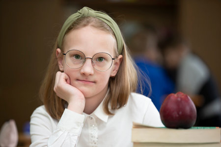 Schoolgirl in glasses at the desk. Girl in the classroom with books and an apple. Secondary school. Back to school.の写真素材