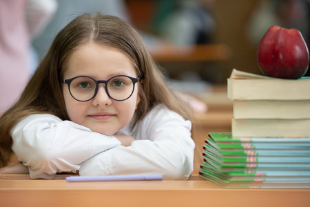 The schoolgirl in glasses rested her head on the desk. Girl in the classroom with books and an apple. Back to school.の写真素材
