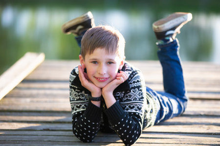 A handsome boy lies on a wooden bridge and smiles. Child in nature.の写真素材