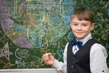 A handsome boy of school age stands at the blackboard, looks at the camera and smiles. Smart student. Back to school.の写真素材