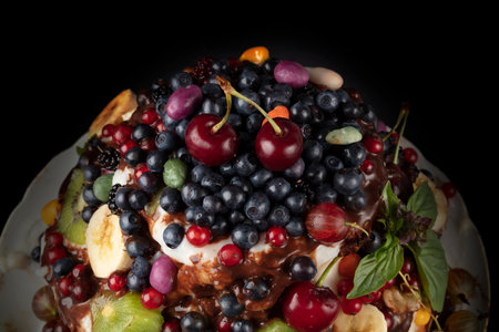 Part of a beautiful cake decorated with various berries and fruits on a dark background.
