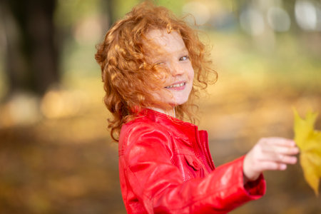 Autumn portrait of a cute smiling little red-haired girl with maple leaves outdoorsの写真素材