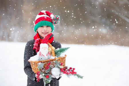 Happy boy in a striped Christmas hat with Christmas toys and decorations under the snowfall.の写真素材