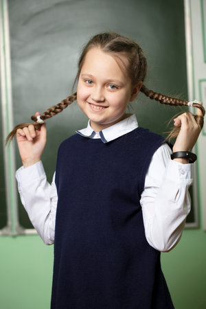 Funny schoolgirl with pigtails, middle school age on the background of the blackboard.の写真素材