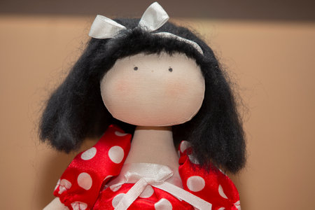 Doll made of handmade fabrics. Portrait of a doll in a red dress with polka dots, only eyes are painted on her face.の写真素材