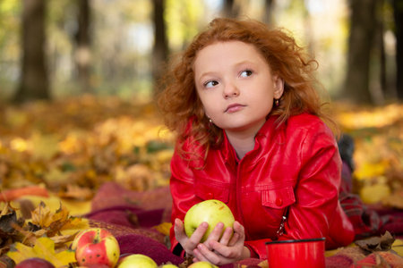 Sad red-haired girl with an apple in the autumn park.の写真素材