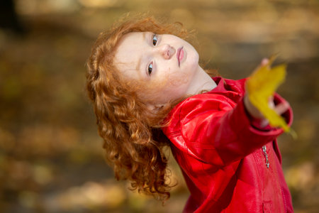 Beautiful little red-haired girl with maple leaves outdoorsの写真素材