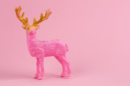 Festive minimalistic Christmas background. On a pink background, a pink deer with golden antlers.の写真素材