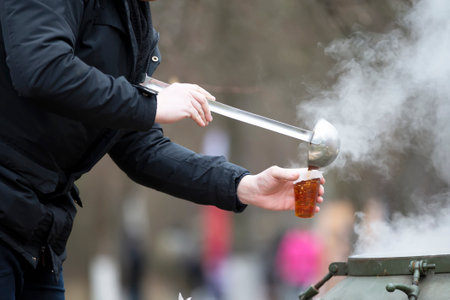 Tea master pours tea in a plastic glass outdoors.