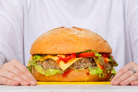 Big burger on the table against the background of female hands.の写真素材