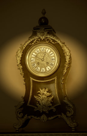 Vintage wooden table clock with nineteenth century golden elements in dark vignette.