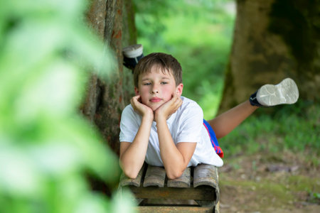 A handsome young boy lies on a bench in the background of a summer garden.の写真素材