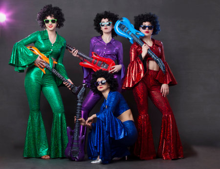 A pop music group sings in a nightclub. Young girls dressed in retro seventies costumes and funny...
