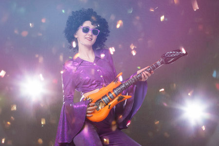 Happy girl pop singer with a toy guitar on the background of shiny confetti. Disco style.