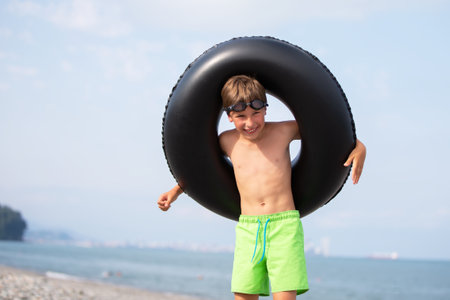 Happy boy with swimming ring and goggles by the sea.の写真素材