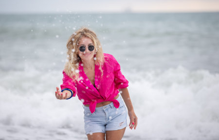 A beautiful woman in sunglasses and a pink shirt splashes sea water.の写真素材