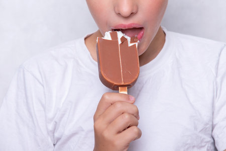 A boy whose face is unrecognizable eats ice cream covered in chocolate.の写真素材