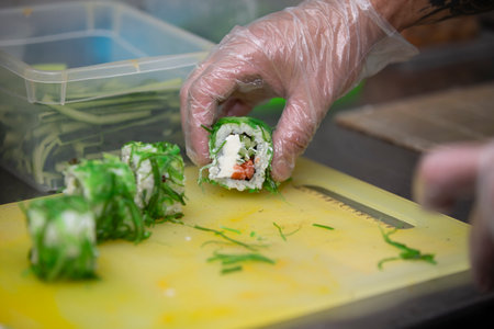 A gloved hand cuts sushi on a cutting board.の写真素材