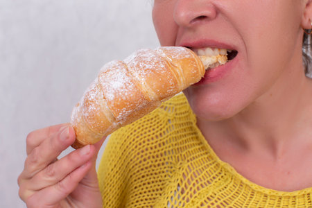 A woman, whose face is not visible, eats a croissant.