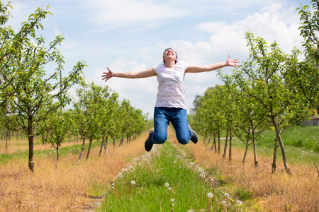 An adult woman rejoices and jumps up against the backdrop of a blooming spring garden.の写真素材
