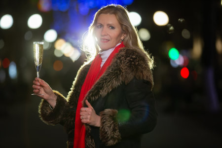 Portrait of a beautiful woman with a glass of champagne in an illuminated evening city. Happy evening celebration moment.の写真素材