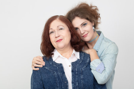 An elderly mother and an adult daughter are looking at the camera. The two hug.の写真素材