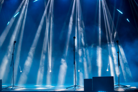 Blurred rays of light from stage spotlights on a blue stage background with microphones. The...