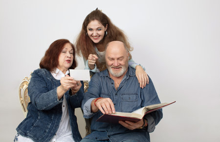 A family portrait of parents and an adult daughter looking at a photo album on a gray background.の写真素材