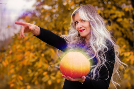 Halloween a woman with gray hair holds a magical glowing pumpkin against the background of an autumn...