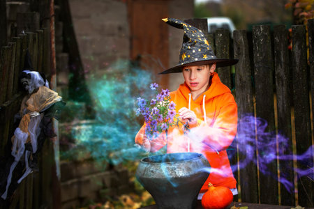A child with a magic bowler hat in a sorcerer's hat performs witchcraft against the background of an old creepy house. The wizard boy at the halloween party.の写真素材