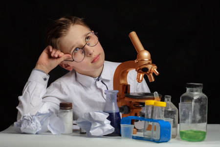 A boy scientist researcher with a microscope is thinking about ideas in the laboratory. Surprise in the laboratory. Science and education.の写真素材