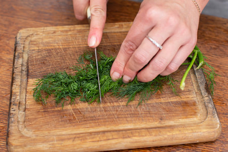 Hands chop dill on a cutting board. Prepare vegetable salad.の写真素材