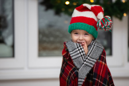 A happy little girl in a Santa Claus hat is wrapped in a warm plaid blanket