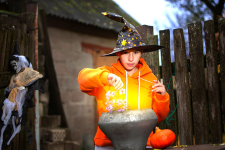 A child with a magic bowler hat in a sorcerer's hat performs witchcraft against the background of an old creepy house. The wizard boy at the Halloween party.の写真素材