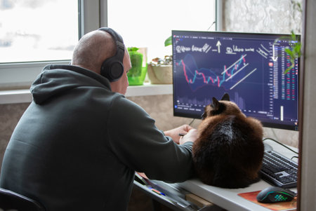 A male trader sits at home at a computer, monitors the schedule on the stock exchange, is engaged in...