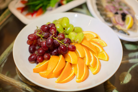 There are sliced fruits, an orange and grapes on a plate.の写真素材
