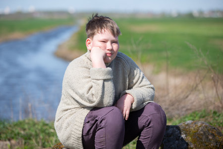 A twelve-year-old boy sits against the backdrop of nature and appears sad.の写真素材