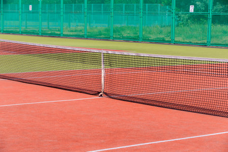 The tennis court is empty with a net and a green fence.