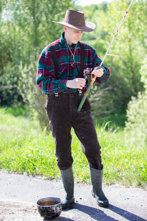 An adult man with a fishing rod and in rubber boots is going fishing.