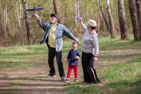 Grandfather, grandmother and grandson launch an airplane during a walk in the forest. The family has a fun time.の写真素材