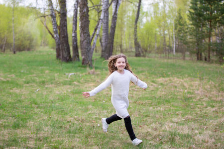 A little girl runs through the spring forest. A child on a walk in the park.の写真素材