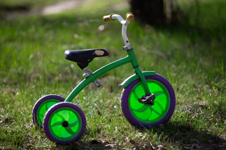 A green tricycle with purple wheels sits on the grass. The tricycle is old and has a vintage look to...