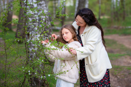 Mom and daughter take a walk in a blooming spring park looking at the trees.の写真素材