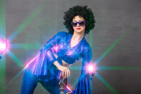 Girl comic pop star posing in black wig with toy guitar on blue background. Rock style of seventiesの写真素材