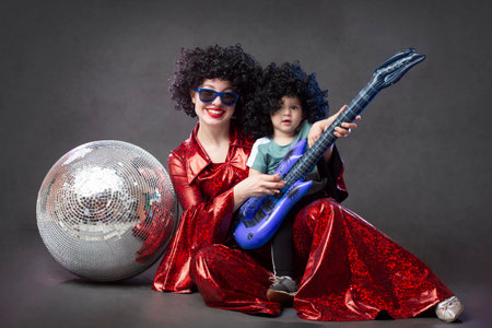 A rock girl in a black wig with a little daughter and a disco ball poses and looks at the camera.