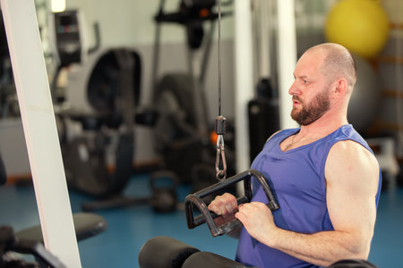 A male athlete is working out on a weight training machine in a gym. He is focused on doing the...