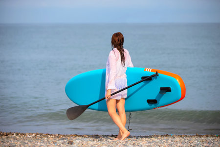 A woman walks along the beach holding a blue boat for sap boarding. A woman enjoys her time on the beachの写真素材