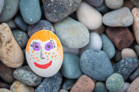 White stone with a painted positive face on a background of gray sea pebbles. Concept of creativity.の写真素材
