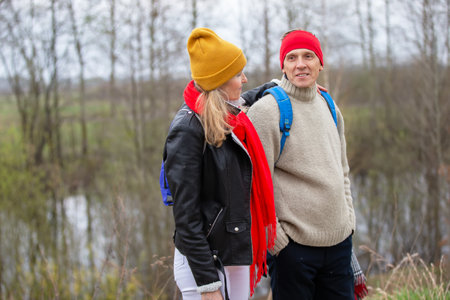 Active elderly Caucasian couple hiking with backpacks enjoying their adventure. They sit with their...