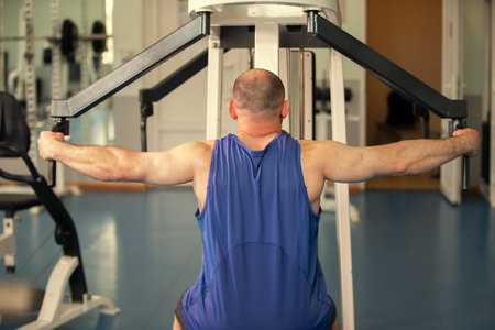 Male athlete exercises on a strength training machine in a gym. Back view.